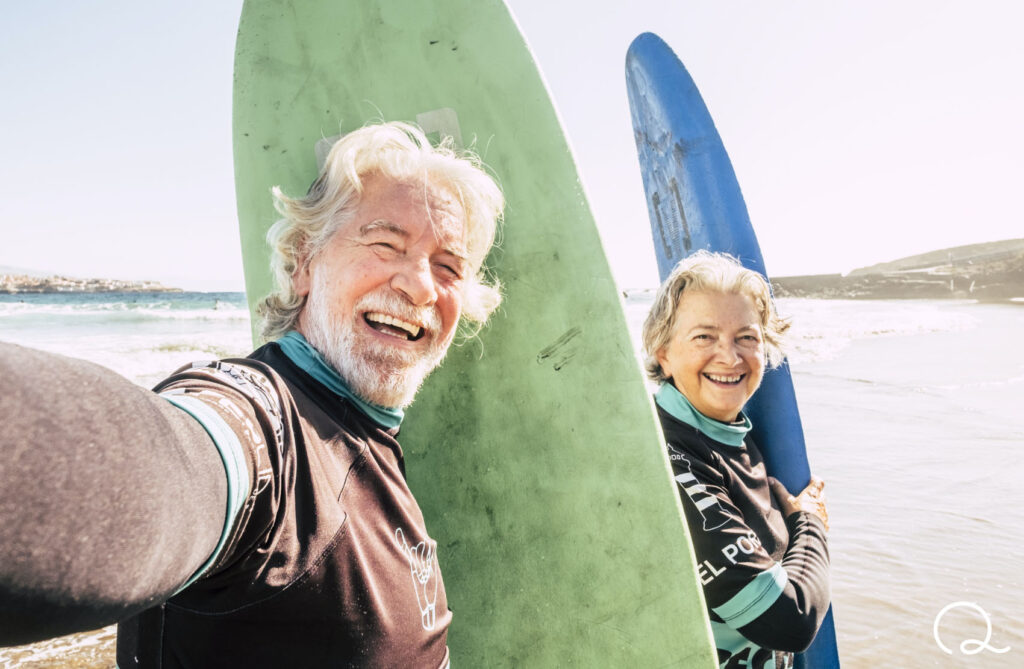 man and woman surfing together on beach smiling at camera